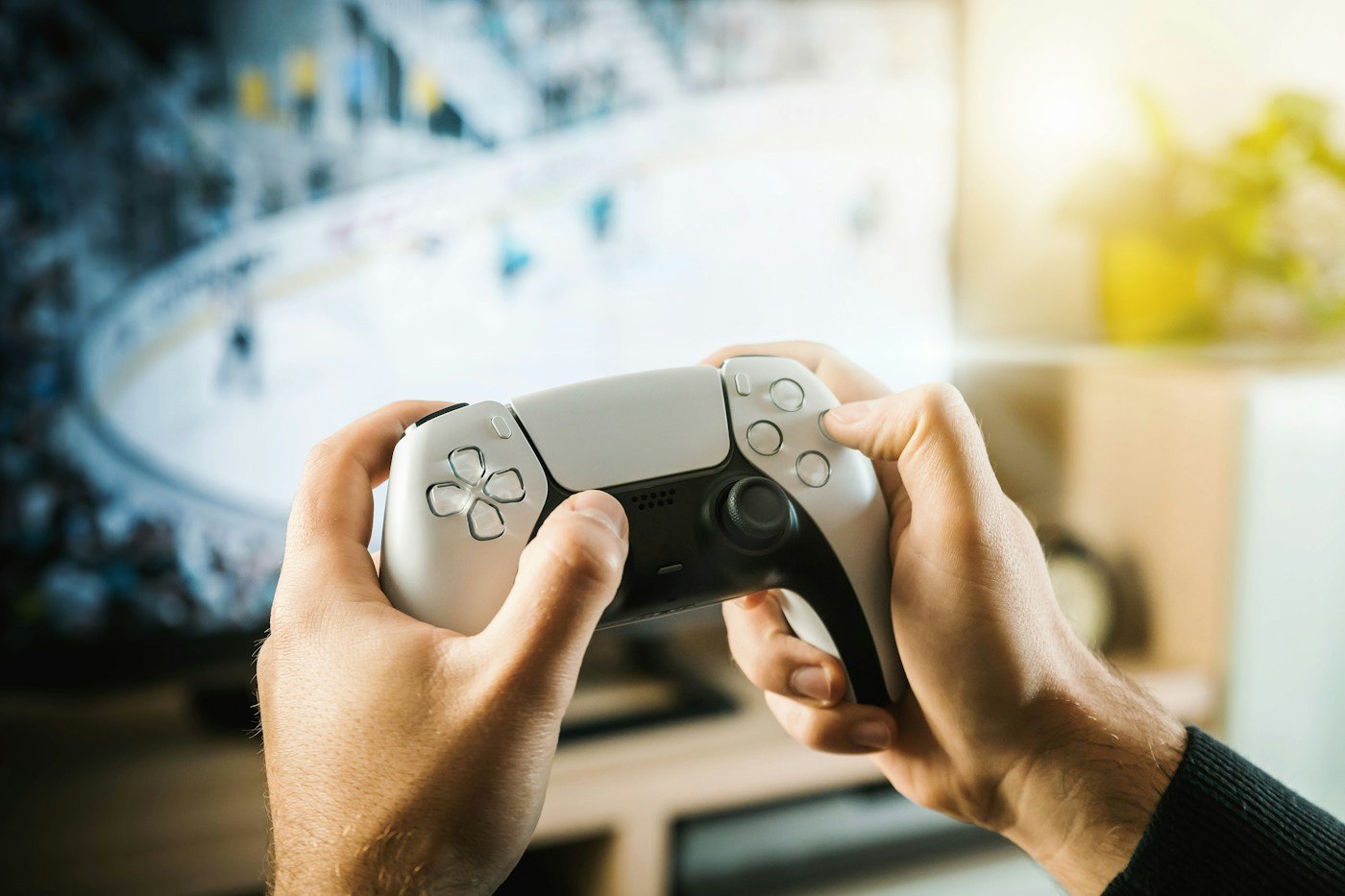 Hands holding a black and white gaming controller in front of a screen