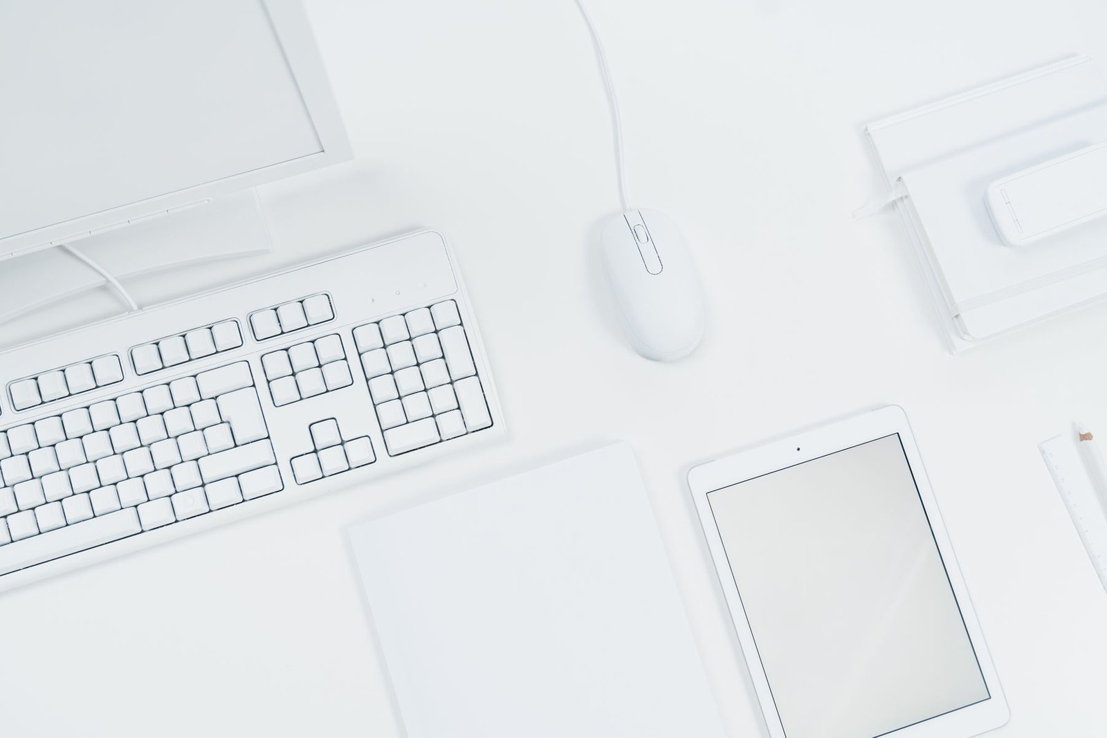 An overhead view of a white keyboard, mouse, computer and tablet