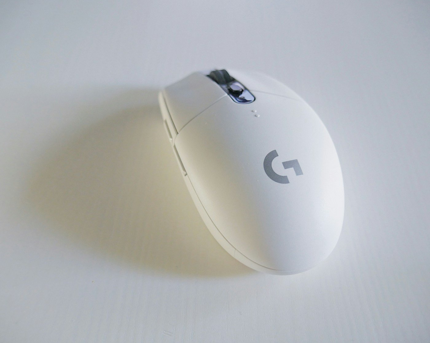 A white wireless computer mouse on a pale desktop